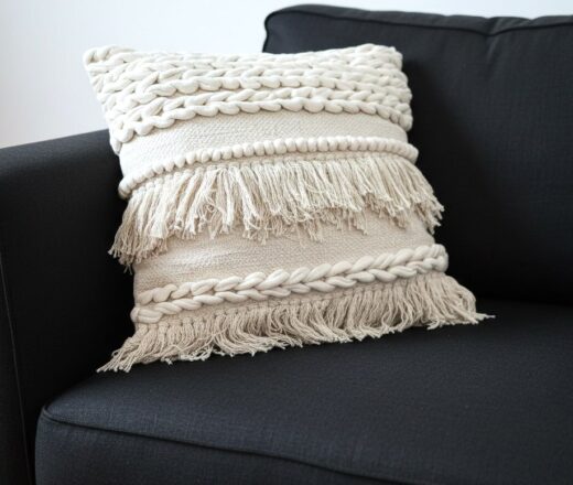 almofada-luxo-balinesa-creme-franjas-apliques A Alma do Estilo Boho: Textura e Aconchego Existem peças que transformam instantaneamente a energia de um ambiente, e esta almofada balinesa é o exemplo perfeito. Com uma estética que transita entre o rústico chique e o estilo boho, ela se destaca pelo contraste sublime entre o tom cru-creme e a força do algodão trabalhado. Os Detalhes que Encantam: Trama Rica: O corpo da peça apresenta diferentes relevos, desde tranças encorpadas que trazem volume até faixas de pontos pipoca que convidam ao toque. Movimento das Franjas: As camadas de franjas desfiadas dão leveza e um ar despojado, quebrando a rigidez de qualquer móvel e trazendo um "movimento estático" muito elegante. Material Natural: Feita em algodão rústico, ela evoca a natureza e a simplicidade, proporcionando um conforto que vai além do visual — é um abraço em forma de decoração. No Décor Posicionada sobre um sofá de linho escuro, ela cria um contraste dramático e sofisticado. O preto do estofado serve como a moldura perfeita para que cada detalhe da trama clara ganhe vida, revelando a complexidade do trabalho manual. "É o toque final para quem busca um refúgio urbano com essência artesanal.